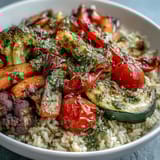 Golden roasted vegetables garnish a hearty Rainbow Roasted Vegetable Bowl served with a drizzle of fresh green sauce.  