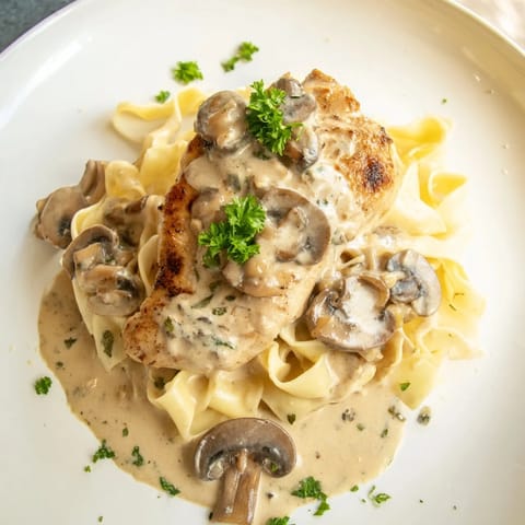 A close-up of tender Creamy Chicken Marsala with rich mushroom sauce and a garnish of fresh parsley on pasta.  