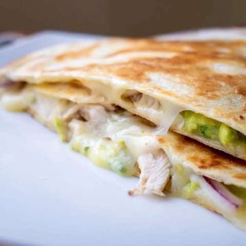 Golden-brown Chicken Avocado Quesadilla wedges stuffed with grilled chicken, creamy avocado mash, and melted cheese.