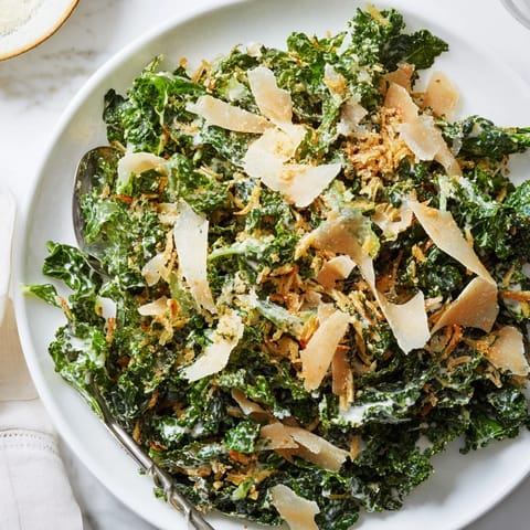 A close-up of vibrant green massaged kale tossed in creamy garlic-Parmesan dressing, topped with golden toasted breadcrumbs and shaved Parmesan.