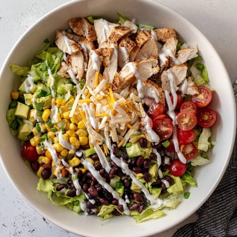 A close-up of Crunchy Taco Chicken Salad with seasoned chicken, black beans, corn, and avocado on crisp romaine, topped with crushed shells and a creamy lime drizzle.