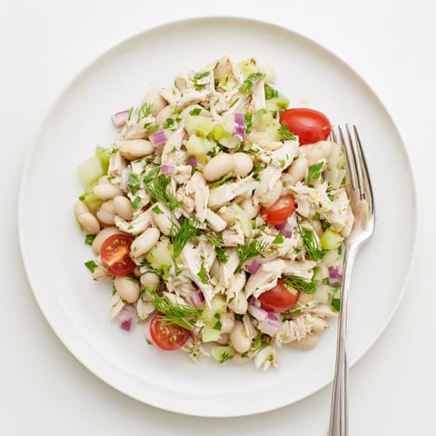 A colorful Mediterranean-inspired bowl of Lemony White Bean Chicken Salad, featuring juicy cherry tomatoes and dill, ready to serve over crisp butter lettuce or with crusty bread.