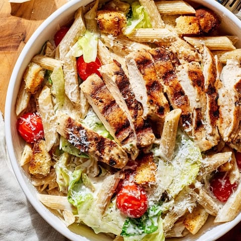 Freshly grilled chicken slices rest atop a vibrant Caesar pasta chicken bowl with crisp romaine and croutons.