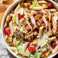 Freshly grilled chicken slices rest atop a vibrant Caesar pasta chicken bowl with crisp romaine and croutons.