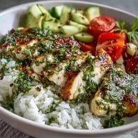 A vibrant Chimichurri Chicken Bowl features grilled chicken over fluffy rice with fresh cucumber, tomatoes, and avocado.